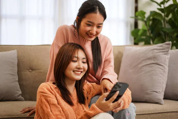 年轻的女同性恋者夫妇穿着毛衣 用智能手机在社交媒体上冲浪 一边吃着美味的爆米花 一边在家里的客厅里共度时光 — 图库照片