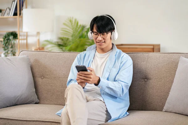 stock image Businessman in casual is sitting on comfortable sofa and wearing headphones to meeting and chatting business information with colleague on smartphone while working in living room at home.