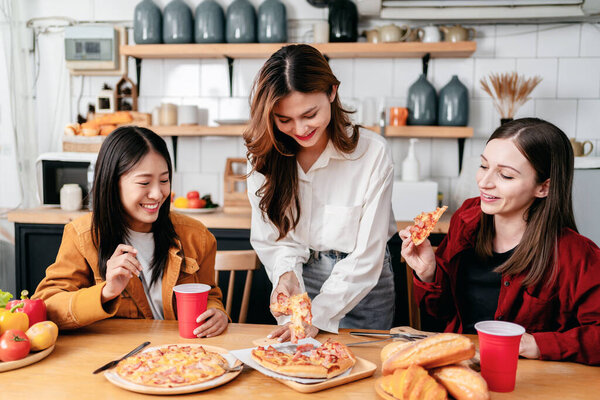 Group of friends eating italian pizza and drinking beverage together while having enjoying with party to celebrate for weekend in the kitchen at home.