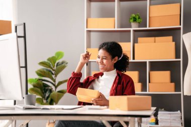 Küçük işletme paket teslimatı konsepti, çevrimiçi satış işlerinde çalışırken başarılı bir şekilde kutlamak için çevrimiçi siparişi kontrol eden Afrikalı girişimci ve kollarını kaldırma.