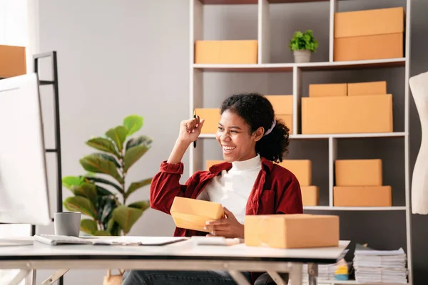 Stock image Small business parcel delivery concept, African entrepreneur checking online order on laptop and raising arm to celebrate for successfully while working about delivery shopping online sales business.