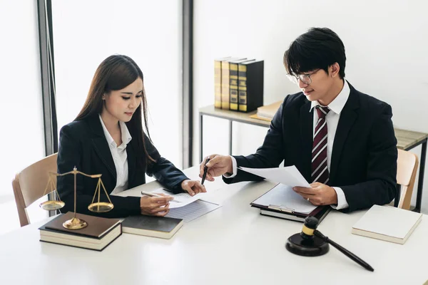 Female lawyer holding business document to reading contract and businessman explaining detail on document to asking about laws and agreements of contracts in law firm office.