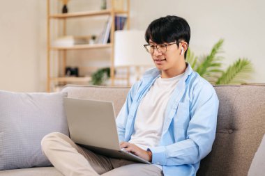 İş adamı rahat bir koltukta oturuyor ve iş arkadaşlarıyla iş görüşmesinde kulaklık takıyor ve evde video konferansında bilgisayarla sohbet ediyor..