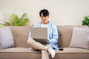 İş adamı rahat bir koltukta oturuyor ve iş arkadaşlarıyla iş görüşmesinde kulaklık takıyor ve evde video konferansında bilgisayarla sohbet ediyor..