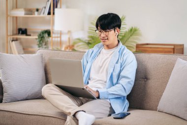 İş adamı rahat bir koltukta oturuyor ve iş arkadaşlarıyla iş görüşmesinde kulaklık takıyor ve evde video konferansında bilgisayarla sohbet ediyor..