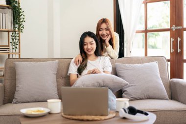 Genç lezbiyen çift dizüstü bilgisayarda film ya da eğlence izlerken evdeki büyük rahat kanepede dinleniyorlar..