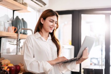 Ev eğlencesi yaşam tarzı konsepti. Mutfak odasında sıradan giyinmiş, dizüstü bilgisayarı olan genç bir kadın. Evde boş zamanlarında arkadaşlarıyla yazışıp sohbet ediyor..