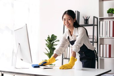 Önlüklü ev hanımı eldiven giyiyor. Evde çalışırken ve temizlik yaparken temizlik yapmak için mikrofiber kumaş kullanıyor..