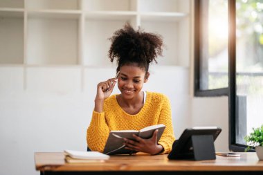 Kazaklı Afro-Amerikalı bir kadın üniversitede bilgi ve eğitimi öğrenirken online tablet dersine çalışmayı ve not defterine not almayı öğreniyor..