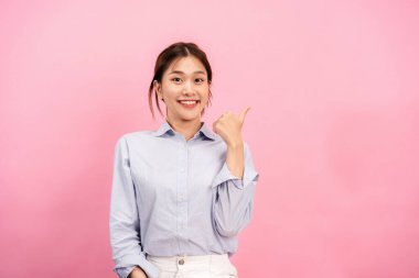Genç Asyalı kadın uzun kollu gömlek giyerken parmaklarıyla bir başparmağını kaldırıyor ve pembe arka planda izole edilmiş bir jesti işaret ediyor..