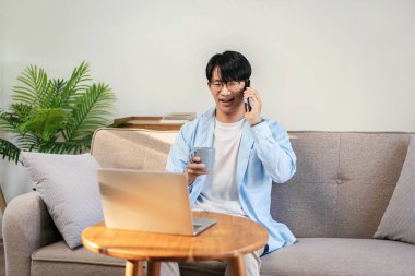 Gündelik iş adamı rahat bir koltukta oturup iş arkadaşıyla konuşurken sıcak çikolata içiyor ve evde dizüstü bilgisayarında iş projesi üzerinde çalışıyor..