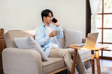 Gündelik iş adamı rahat bir koltukta oturup iş arkadaşıyla konuşurken sıcak çikolata içiyor ve evde dizüstü bilgisayarında iş projesi üzerinde çalışıyor..