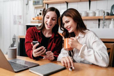 İki genç kadın iş bilgilerini araştırmak ve birlikte veri okumak için akıllı telefonu kullanıyor. Kahve içerken ve evde dizüstü bilgisayarla çalışırken yeni proje işleriyle ilgili beyin fırtınası yapıyorlar..