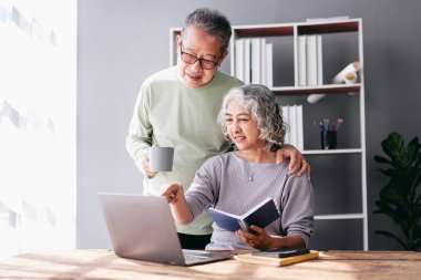 Üst düzey bir çift, evde oturma odasında, hayat sigortası satın almak ve internetten alışveriş yapmak için laptoptan bilgi okurken kahve içip kucaklaşıyorlar..