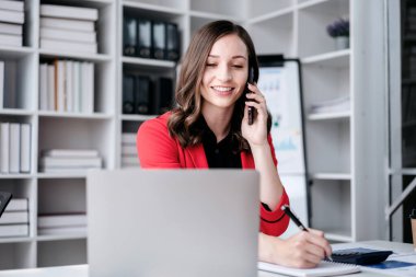 İş kadını akıllı telefon kullanarak strateji analizi ve ofiste yeni iş planları yaparken bilgisayardan iş verilerine bakıyor..