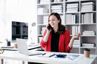 İş kadını akıllı telefon kullanarak strateji analizi ve ofiste yeni iş planları yaparken bilgisayardan iş verilerine bakıyor..