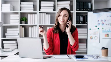 İş kadını akıllı telefon kullanarak strateji analizi ve ofiste yeni iş planları yaparken bilgisayardan iş verilerine bakıyor..