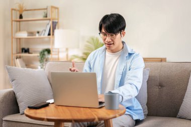 İş adamı rahat bir koltukta oturup iş bilgisini iş arkadaşlarıyla konuşurken kulaklık takarak evde video konferansında bilgisayar kullanıyor..