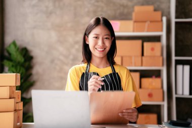 Küçük işletme paket teslimatı konsepti, panoya bilgi yazan kadın girişimci müşteriler için sevkiyat için ürün paketlerken ve çevrimiçi satış ticareti hakkında çalışırken.