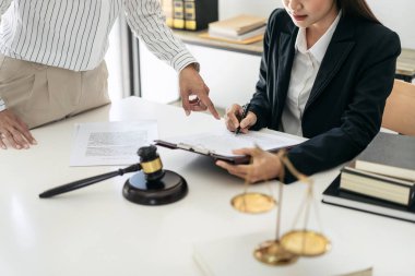 Kadın avukat iş sözleşmesi okuyor ve müvekkil ile yapılan sözleşmeler ve yasalar hakkında tavsiyelerde bulunurken, iş kadını da hukuk bürosundaki ayrıntılara işaret ediyor..