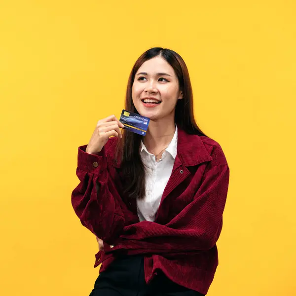 黄色の背景に隔離されたオンラインショッピングの準備を夢見ながら赤いジャケットと大きな笑顔を身に着けている若いアジアの女性 — ストック写真