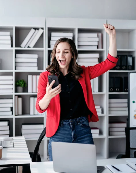 Accounting business concept, Accountant woman reads good news on smartphone with excited and raising fist to celebrate achievement while working about investment with business planning finance.