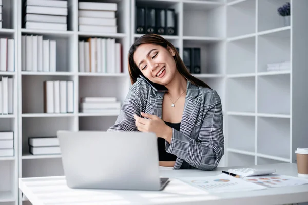 Accounting business concept, Accountant woman using smartphone to talking with partners and typing finance data on laptop while working to analyzing about investment with business planning finance.
