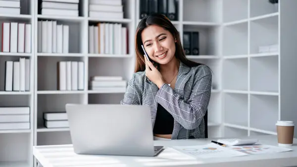 Accounting business concept, Accountant woman using smartphone to talking with partners and typing finance data on laptop while working to analyzing about investment with business planning finance.