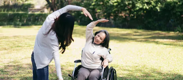 Senior on wheelchair and daughter family concept, Young asian woman exercise with mother on wheelchair in the garden while senior woman and daughter relaxation with enjoying together.