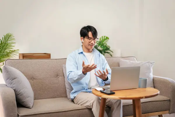 Businessman in casual is sitting comfortable sofa and wearing headphones to explaining business information with colleague while using laptop to meeting in video conference at home.