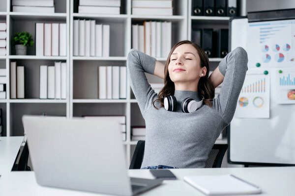 Businesswoman with technology lifestyle concept, Businesswoman wearing headphone in her neck and holding hands behind the head to stretching with close eyes while relaxation after working.