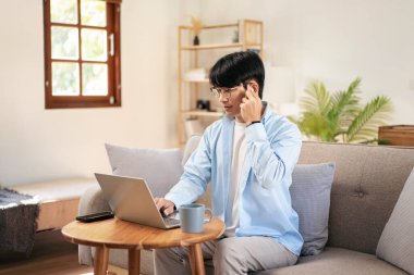İş adamı rahat koltukta oturuyor ve kulaklık takıyor iş bilgisini meslektaşına anlatırken aynı zamanda evde video konferansında bilgisayar kullanıyor ve sohbet ediyor..