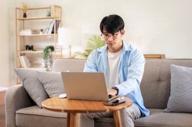 Gündelik iş adamı rahat bir koltukta oturup yeni iş için düşünceli bir fikirle evde iş projesi hakkında bilgi yazmak ve çalışmak için dizüstü bilgisayar kullanıyor..