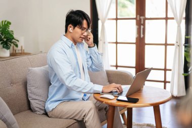 İş adamı rahat koltukta oturuyor ve kulaklık takıyor iş bilgisini meslektaşına anlatırken aynı zamanda evde video konferansında bilgisayar kullanıyor ve sohbet ediyor..