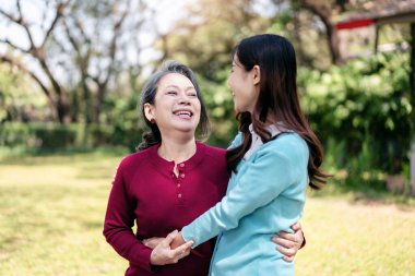 Yaşlı ve kız aile kavramı, Asyalı genç bir kadın annesine gülümseyip sarılırken, yaşlı bir kadın ve kızı bahçede konuşurken dinleniyorlar..