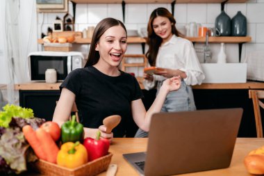 İki genç kadın yemek tarifini laptopta birlikte öğreniyor ve izliyorlar. Evde modern mutfağın tadını çıkararak sağlıklı bir yemek hazırlıyorlar..