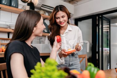 İki genç kadın ellerinde domates ve ekmek ile birlikte sağlıklı yemek pişirirken aynı zamanda evde modern mutfakta keyif ve rahatlıkla vakit geçiriyorlar..