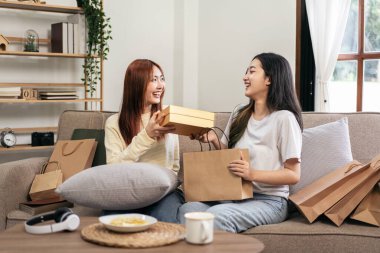 Genç bayan lezbiyen heyecanlı bir yüz ifadesi takınırken kız arkadaşından hediye alıyor ve evdeki büyük rahat kanepede dinleniyor..