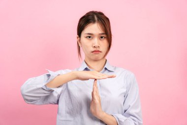 Uzun kollu gömlek giyen Asyalı genç bir kadın ve hayal kırıklığına uğramış bir yüz. İki elini de pembe arka planda izole edilmiş bir jest yapmak için kullanıyor..