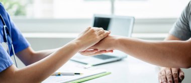 Bir doktor ve hasta tıbbi bir ortamda el sıkışıyor. Hasta gri bir gömlek giyiyor.