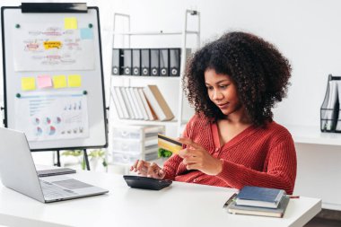 Bir kadın kredi kartını bir şeyin parasını ödemek için kullanıyor. Bilgisayarı ve hesap makinesi olan bir masada oturuyor.