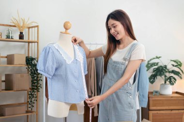 Kadın moda tasarımcısı manken elbisesi giyiyor ve ölçü bandıyla gömlek ölçüyor. Bu sırada stüdyoda yeni bir kıyafet koleksiyonu tasarlıyor..