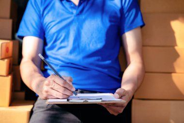 Mavi gömlekli bir adam panoya yazı yazıyor. Bir yığın kutunun üzerinde oturuyor.