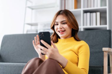 Bir kadın kanepede oturuyor ve cep telefonuna bakıyor. Gülümsüyor ve mutlu.