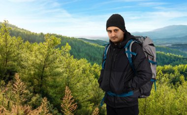 Genç adam ağır bir sırt çantasıyla dağlarda yürüyüş yapıyor ya da güneşli bir günde yürüyüş yapıyor. Tek başına yolculuk mu yoksa yolculuk tutkusu mu?. 