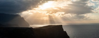 Güneş batarken Madeira 'nın kuzey sahilinin panoramik fotoğrafı. Atlantik Okyanusu 'na düşen sarp kayalıklar dramatik bulutlar ve güneş ışınlarıyla.