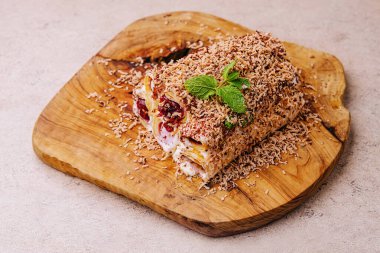 Cake from rolled pancakes with cream, cherries and grated chocolate on wood