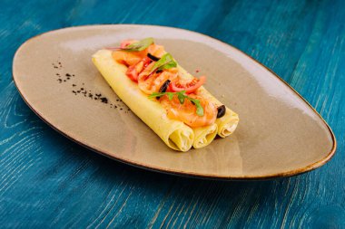 Delicious thin pancakes with salmon and sour cream on plate