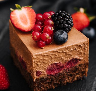 Delicious chocolate cake decorated with fresh berries on wooden black table
