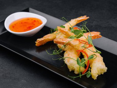 Kızarmış karides tempura ve siyah taş tabakta acı biber sosu.